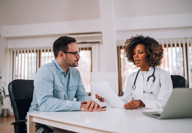 A black woman doctor talking to a white male patient.