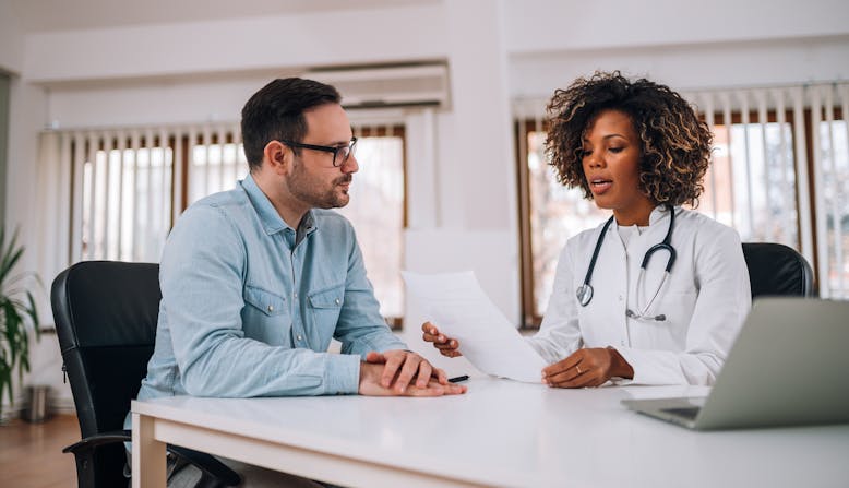 A black woman doctor talking to a white male patient.