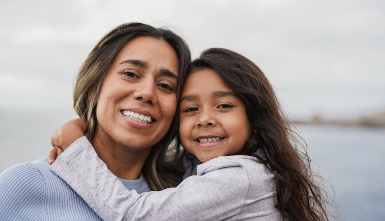 A young Latinx girl hugging her mom.