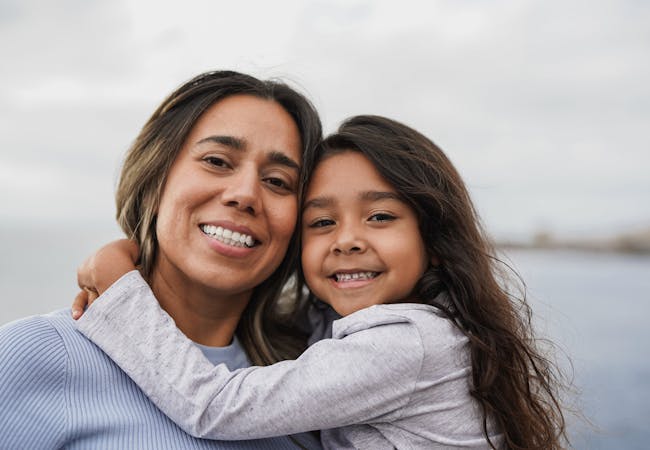 A young Latinx girl hugging her mom.