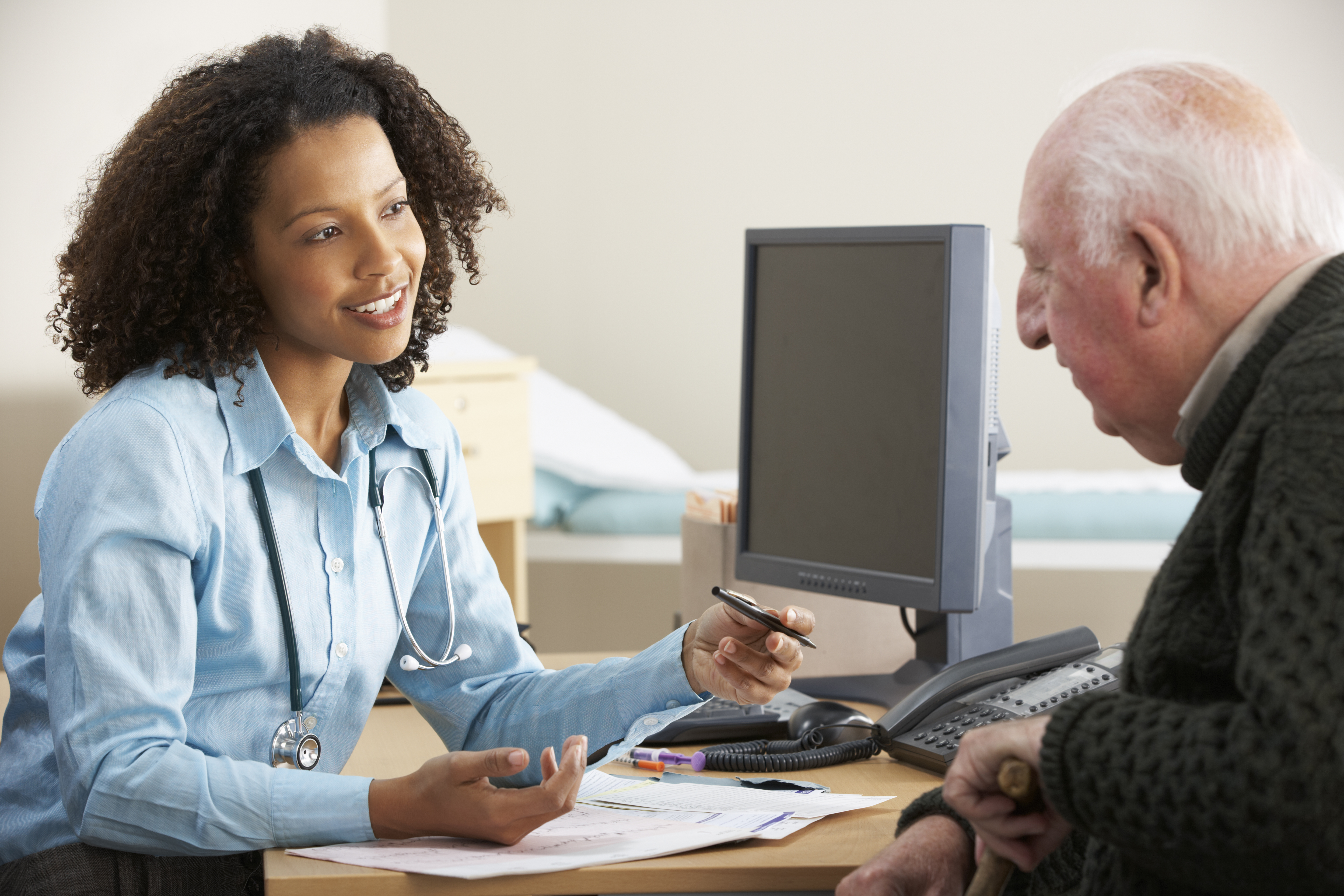 A man speaks to a doctor at her desk in front of a computer.