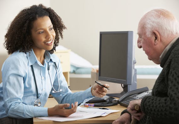 A man speaks to a doctor at her desk in front of a computer.