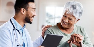 A male doctor shows an elderly woman patient her chart on a tablet.