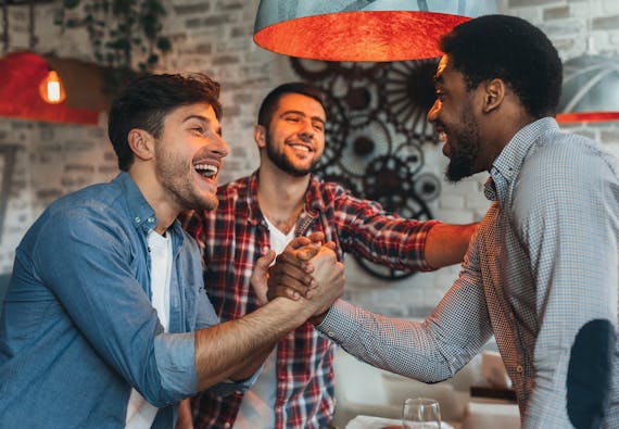 Two men lock hands and laugh with a third man standing by.
