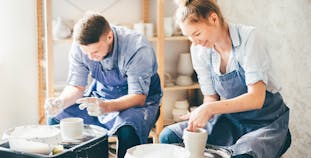 A man and a woman at pottery wheels in a studio.