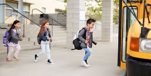 Two children with backpacks getting on a school bus.
