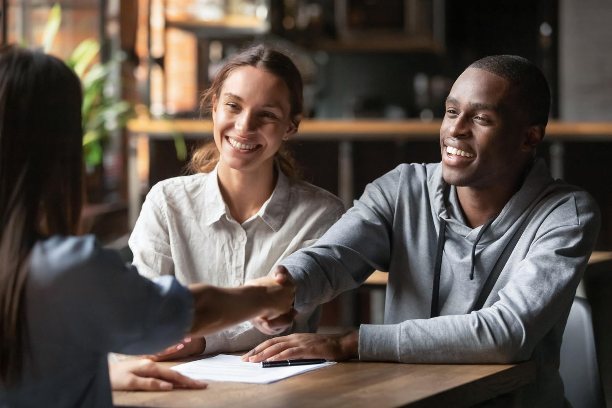 A happy couple meets with an advisor and shakes her hand.