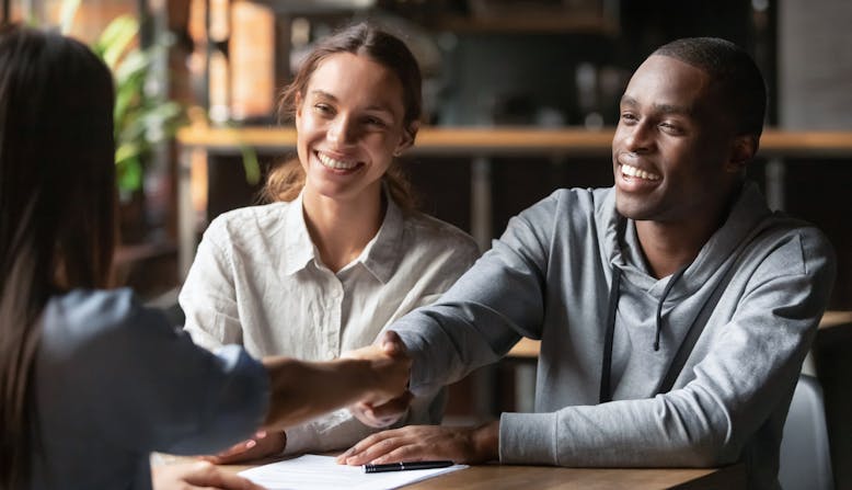 A happy couple meets with an advisor and shakes her hand.