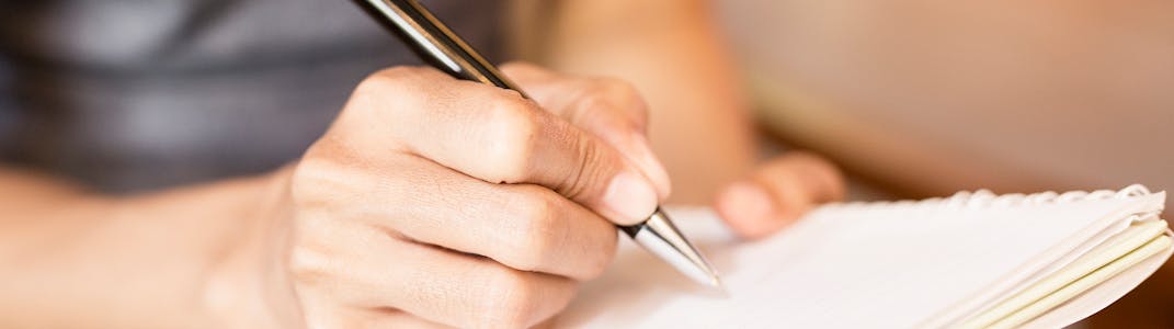 A woman writes in a notebook with a pen.