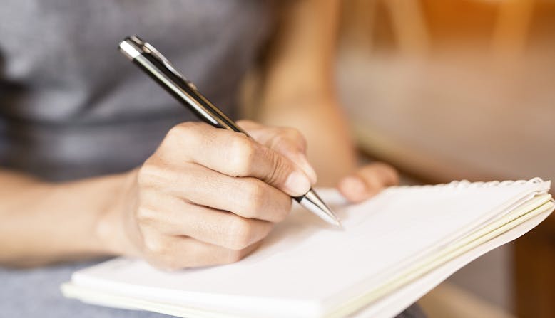 A woman writes in a notebook with a pen.