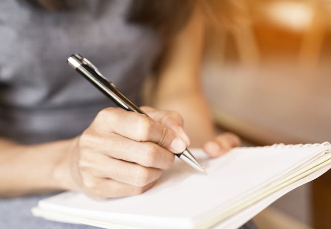 A woman writes in a notebook with a pen.