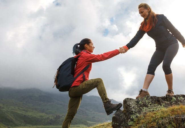 Two women helping each other climbing a mountain.