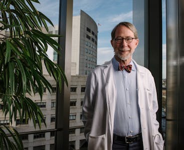Philip Mease smiles in front of a large window while wearing a lab coat and bow tie.