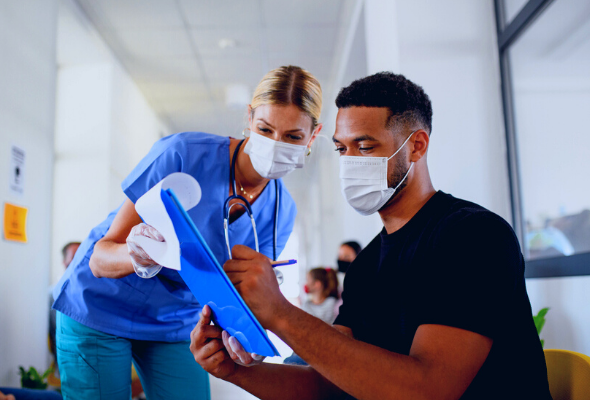 A health care professional reviews information on a clipboard with a patient in the waiting room of a medical office.