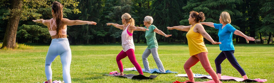 A group of women in a park exercise on yoga mats.