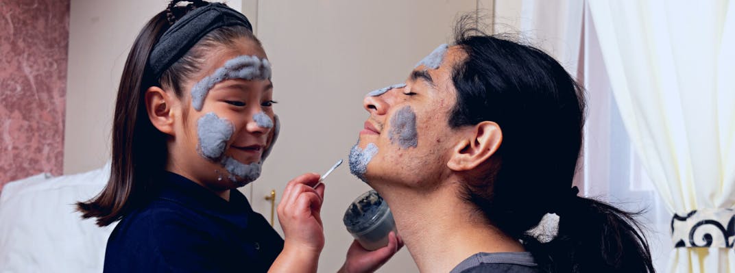 A father and daughter put on face masks together.