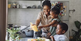 A Black woman teaching her two children how to cook.