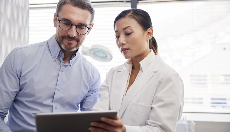 A female health care professional looking at an iPad with a male health care professional.
