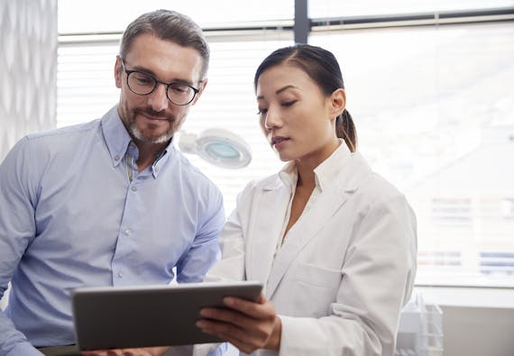 A female health care professional looking at an iPad with a male health care professional. 