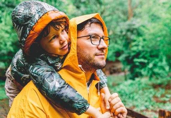 A father holds his son on his shoulders on a rainy day in the woods.