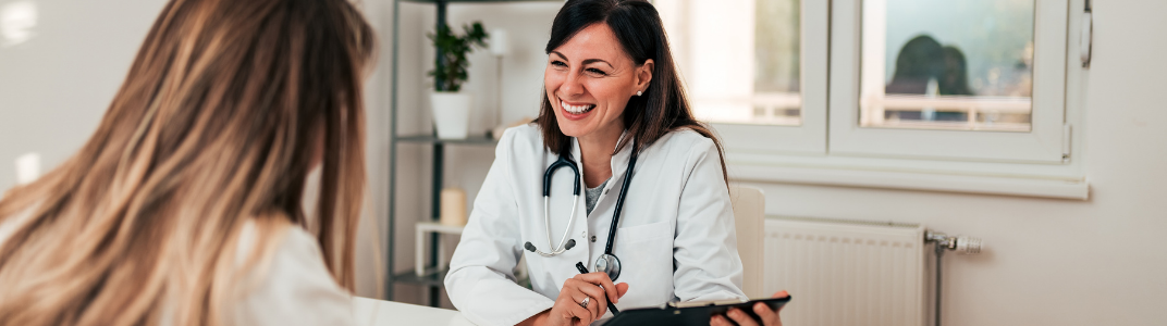 A doctor smiles at her patient as she writes on a clipboard.
