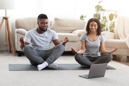 A man and woman meditating on a yoga mat while looking at a laptop.