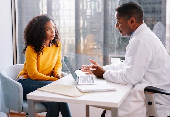 A male doctor discusses with a female patient in an office.