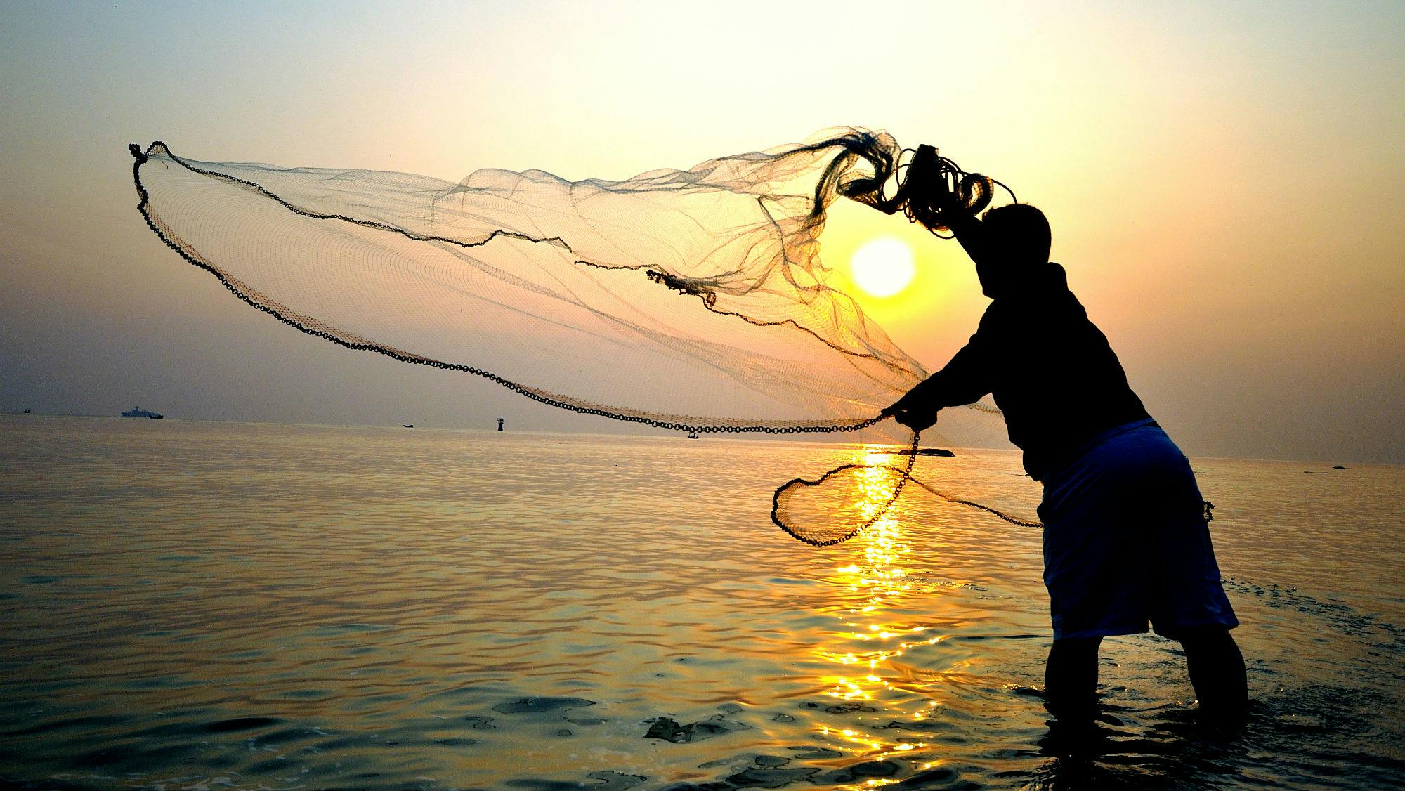 man throwing fishing net into sea 