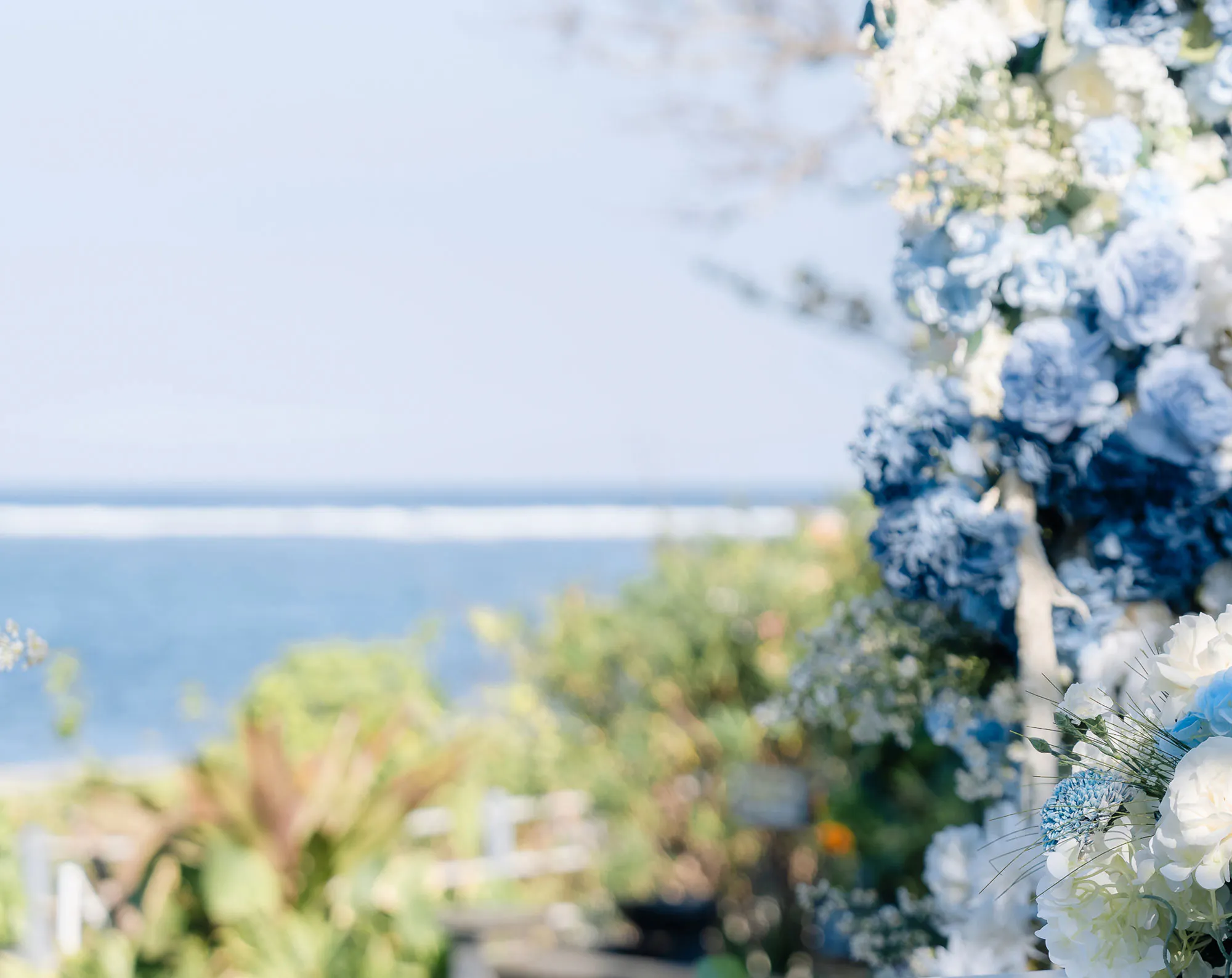 Elegant Nusa Dua Bali wedding ceremony arch adorned with blue and white flowers, with tropical garden and Indian Ocean views in the background