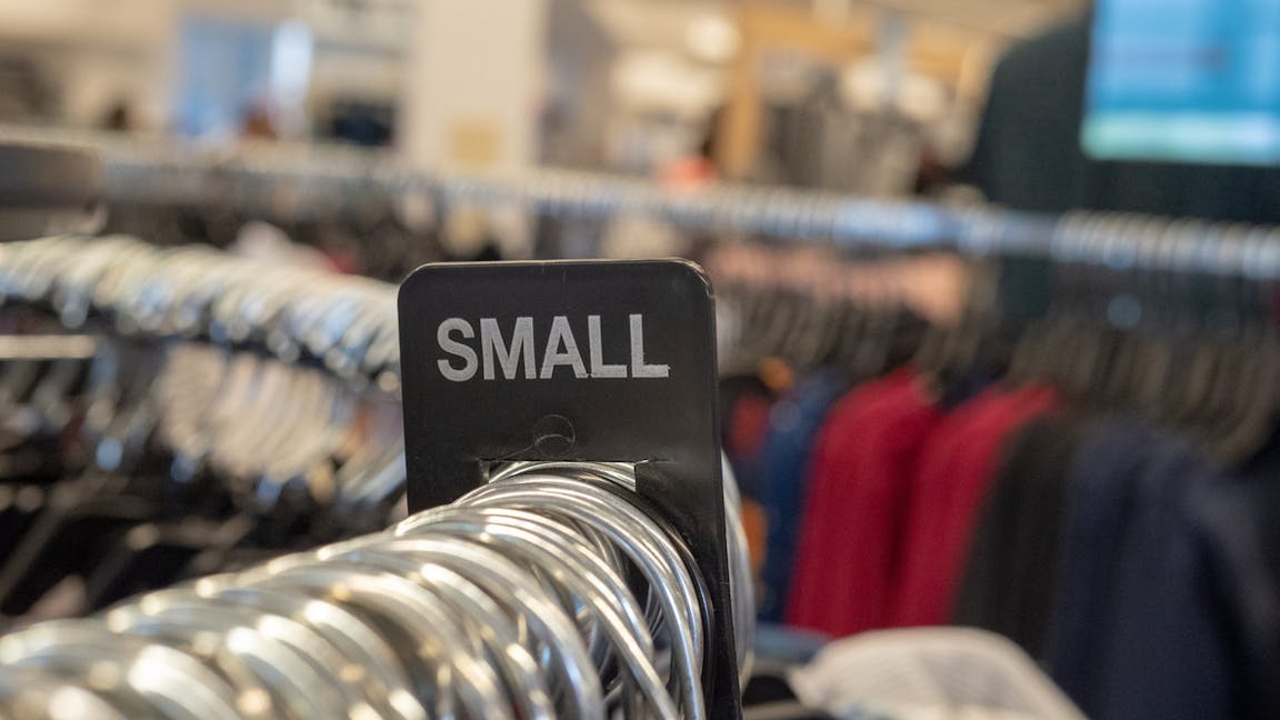 Small clothes section sign on steel hanging rack with hangers in a department store