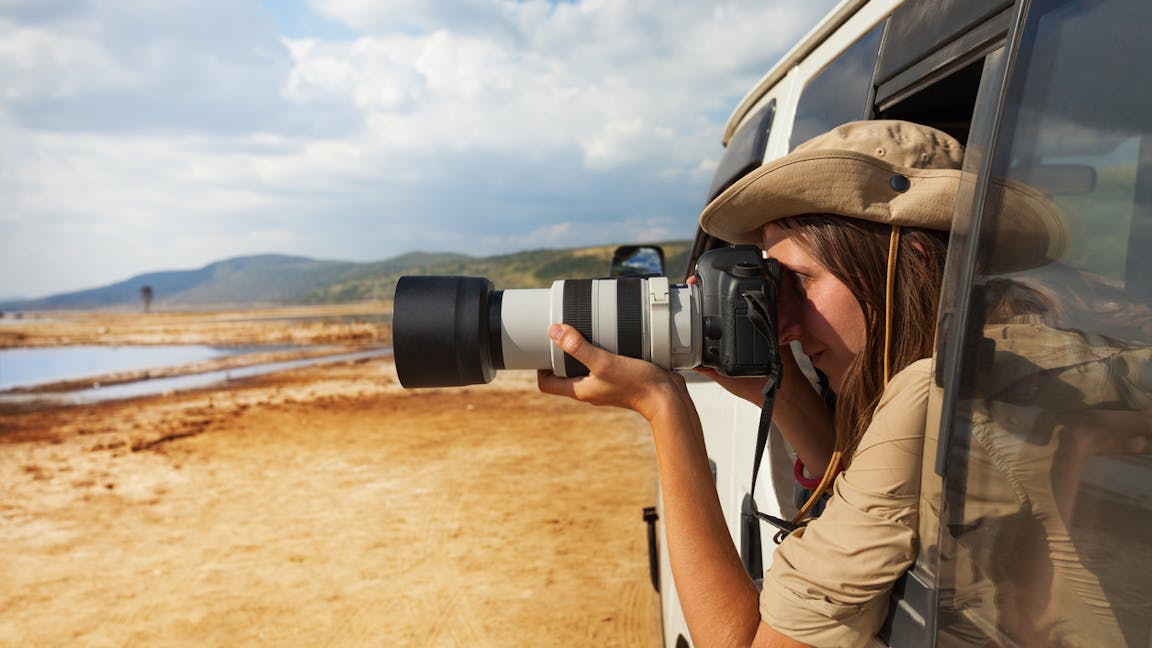 Side view portrait of young woman taking photo of Kenyan lake Nakuru from the open window of safari jeep