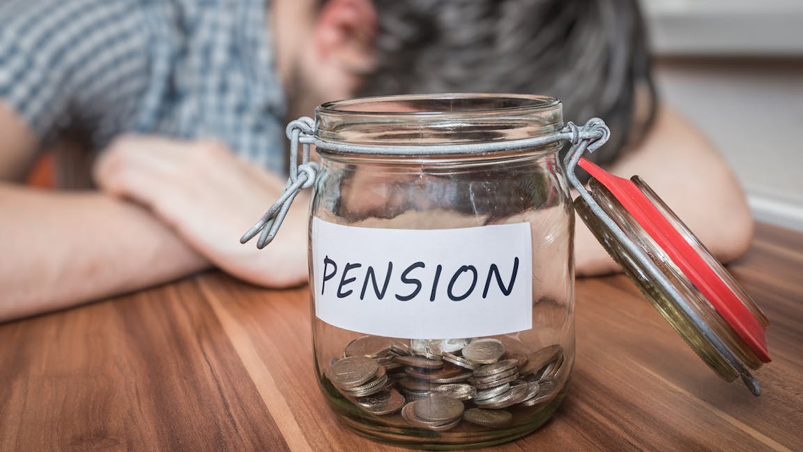 Depressed man lying on table worried about pensions. A pension savings in jar in front.