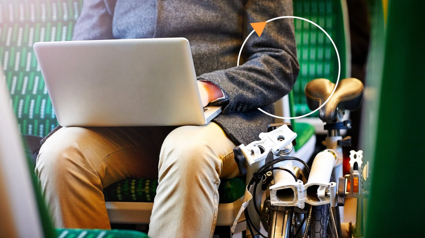 Businessman sitting on train with his folding bicycle using laptop