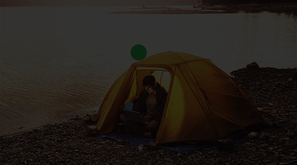 Man writing in a notebook inside a tent next to the lake