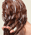 The view from behind as a woman runs Nutrafol Strand Defender Conditioner through long auburn hair with her fingers.