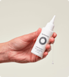 Hand holding a small white squeeze tube bottle of Nutrafol Stress Reliever Essence that is dripping in clear liquid.