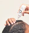 Hands applying Nutrafol Stress Reliever Essence—a clear liquid in a white bottle with nozzle—to the part line of their scalp.