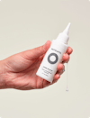 Hand holding a small white squeeze tube bottle of Nutrafol Stress Reliever Essence that is dripping in clear liquid.