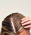 Woman's scalp with exfoliating scalp mask applied to the hair part line.