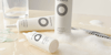 3 white bottles with a label of black circular rings on a beige countertop covered in a green gel, clear liquid, and shampoo suds.