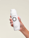 Person holding Nutrafol Root Purifier Shampoo with foaming gel on the bottle and fingers.