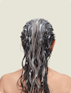 The back of a brunette woman's head with conditioner in her hair.