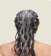 The back of a brunette woman's head with conditioner in her hair.