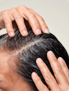 Two hands exfoliating scalp mask into scalp and hair.