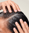 Two hands exfoliating scalp mask into scalp and hair.