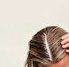 Woman's scalp with exfoliating scalp mask applied to the hair part line.
