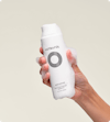 Person holding Nutrafol Root Purifier Shampoo with foaming gel on the bottle and fingers.