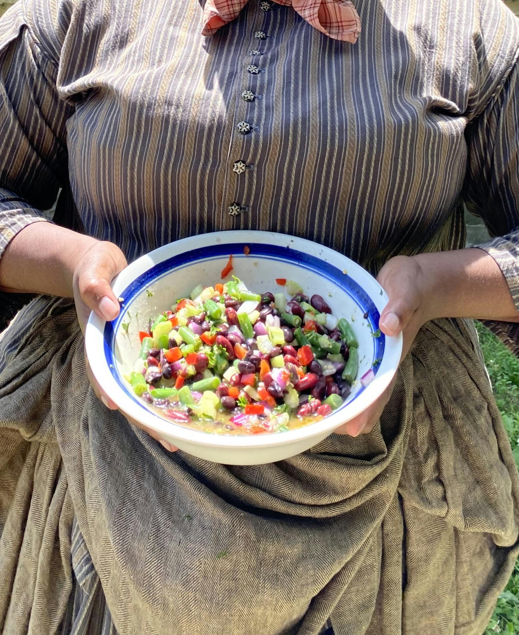 a living historian holding a white bowl with Marcus Garvey bean salad