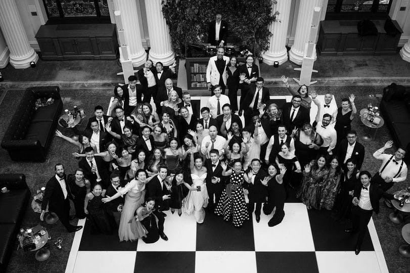 wedding party shot from above in the reading room showing a crowd of guests looking up and waving at the camera