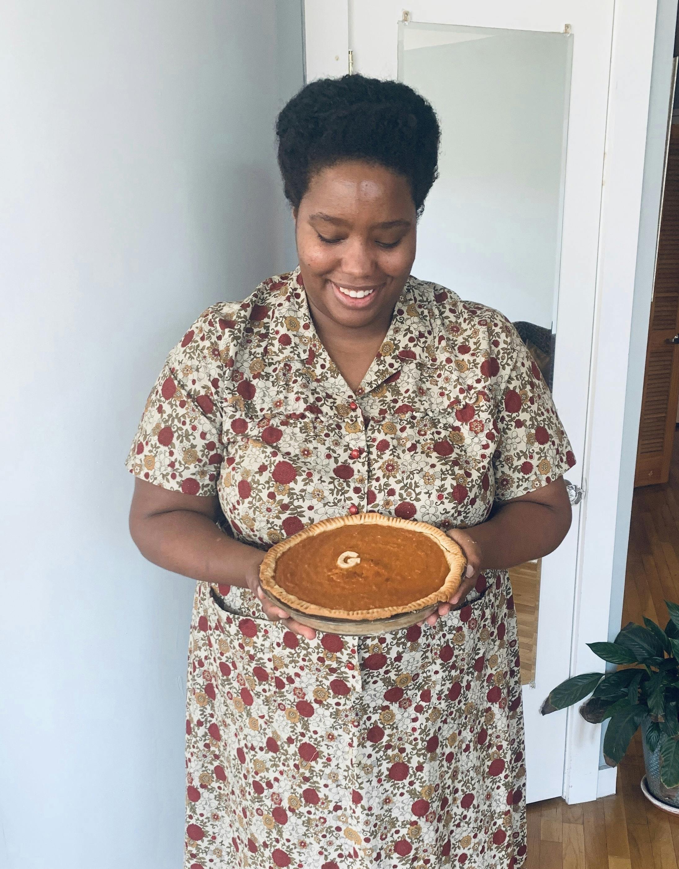 Cheyney McKnight portraying George Gilmore—she's wearing a 1940s housedress and holding a sweet potato pie.
